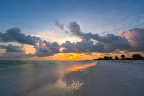 Beach sunset with dramatic clouds reflected on calm ocean water Stock Photos