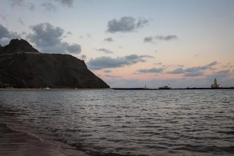A beach at sunset with a ship in the background and hillside on the left Stock Photos