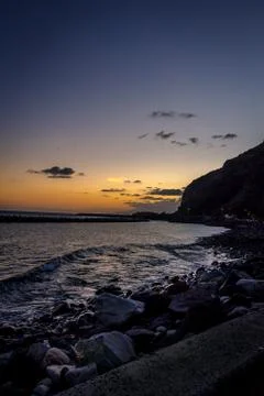 A beach at sunset with a ship in the background and hillside on the left Stock Photos