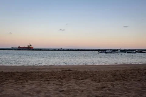 A beach at sunset with a ship in the background Stock Photos