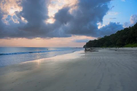 Beach sunset with soft waves, cloudy sky and sandy shoreline Stock Photos