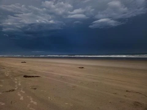 Beach at sunset under dark clouds Stock Photos