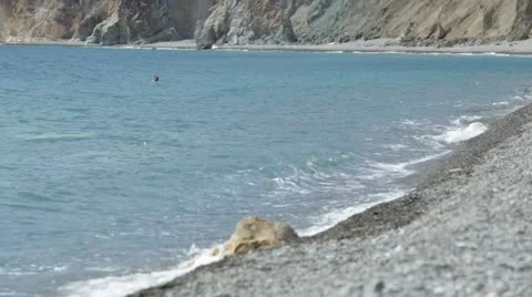 Beach, surf. Stone pebbles. One swimmer among the waves. Stock Footage 22155627