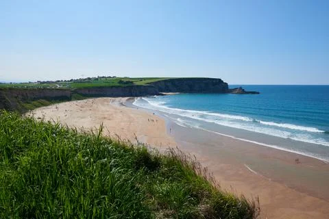 A beach surrounded by cliffs and vegetation under a clear sky. Stock Photos