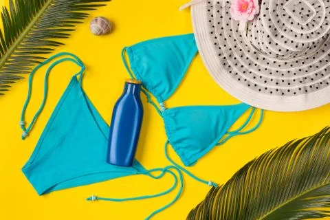 Beach theme on the yellow background. Sunscreen, hat, palm leaves, swimsuit   Stock Photos