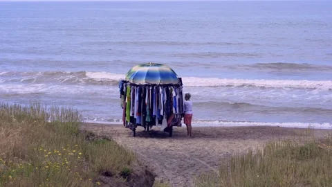 Beach trader selling clothes to a local tourist at Marina di Latina, Italy Stock Footage 243432941