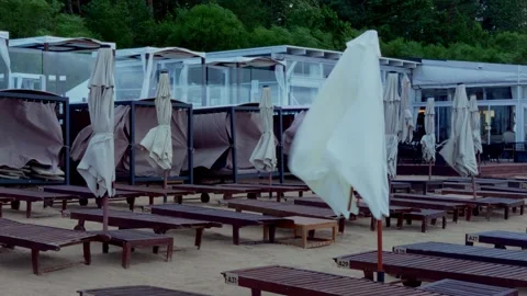 Beach umbrella falling down in strong wind by empty sun loungers in Jurmala Stock Footage 344355548