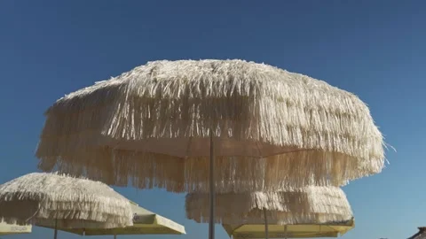 A beach umbrella made of soft straw develops in a weak wind on a blue-pore beach Stock Footage 201546856