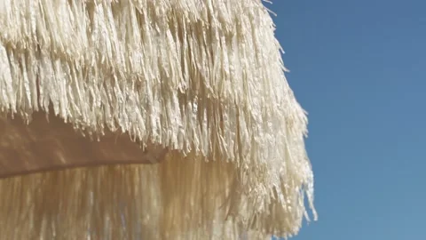 A beach umbrella made of soft straw develops in a weak wind on a blue-pore beach Stock Footage 201546901
