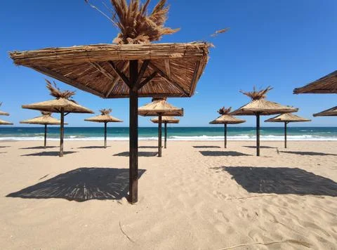 Beach umbrellas covered with straw on an empty sunny sea beach. Beach vacatio Stock Photos