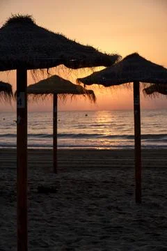 Beach umbrellas at sunset with waves breaking on the shore during evening hou Stock Photos