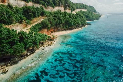 Beach under cliffs with turquoise quiet ocean in Bali. Aerial view Stock Photos