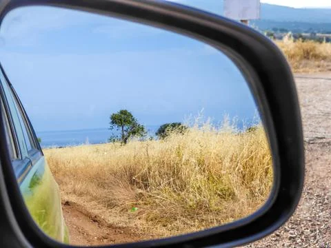 A beach view seen in the side mirror of a car. Driving through a graveled roa Foto stock