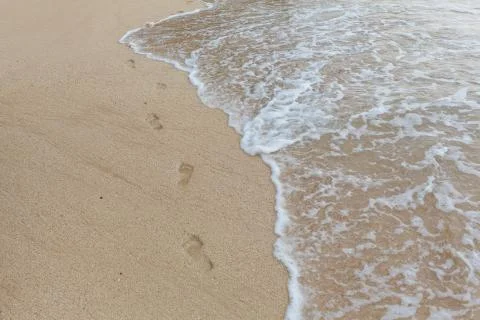 Beach, wave and footprints at sunset time Stock Photos