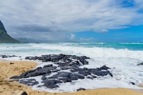 Beach with waves hitting rocks, mountain in background Stock Photos