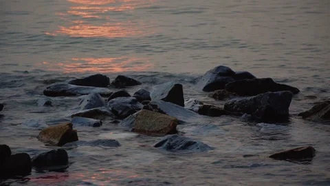 Beach waves hitting rocks with sun reflection during sunset. Stock Footage 99810028