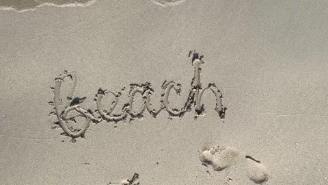Beach word written in sand with footprints on sunny day Stock Footage 329966588