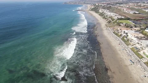 Beachfront homes, waves, people walking, surfers on the California coastline Stock Footage
