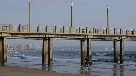Beachfront waves gently washing up the shore under the pier while walking Stock Footage 80591912