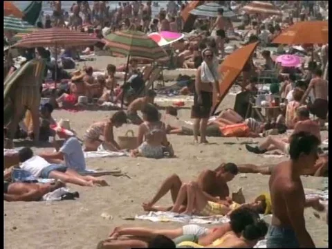 Beachgoers relax on crowded beach during a hot summer day in the 1980s. Stock Footage 75275308