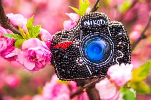 A bead brooch in the shape of a camera. Handmade brooch on the background of blo Stock Photos