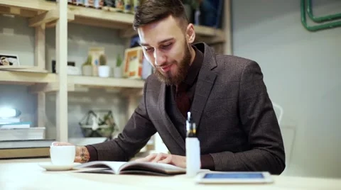 Beadrded man is reading magazine with e-cigarette vape in cafe Stock Footage 56891959