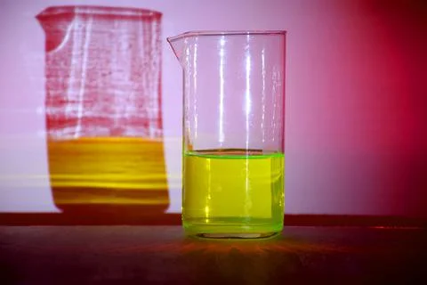 A beaker with glowing green liquid casting colorful shadows on a pink background Stock Photos