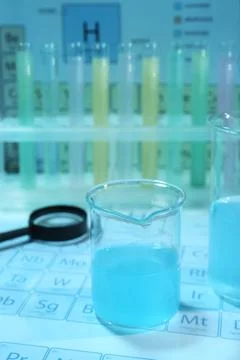 Beaker with liquid, test tubes and magnifying glass on periodic table of ch.. Stock Photos