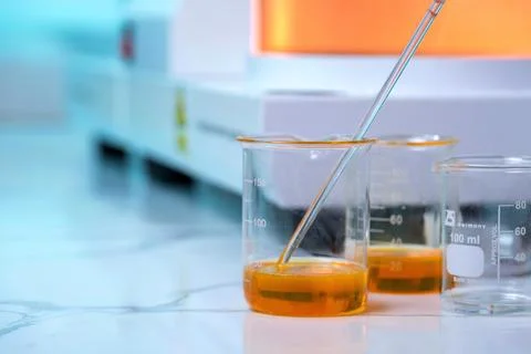 A beaker with a yellow liquid in it is next to two other beakers Stock Photos