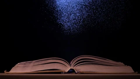 A beam of light illuminates the pages of an open book on a table in a dark 動画素材 148869490