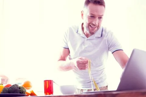 Beaming bearded man using his laptop while watching program about health and 库存照片