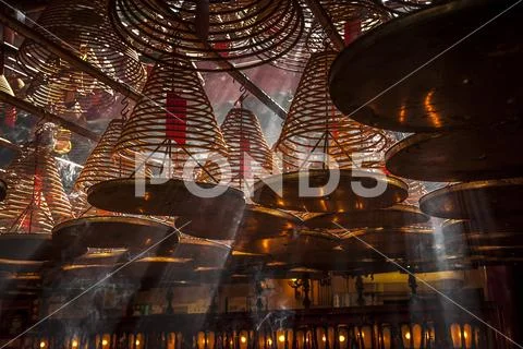 Beams of light streaming into Man Mo Temple past the large incense coils hanging Stock Photos