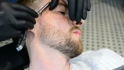 Beard cut with straight razor shave. Close up of shaving beard in barber shop. M Stock Footage 90675555