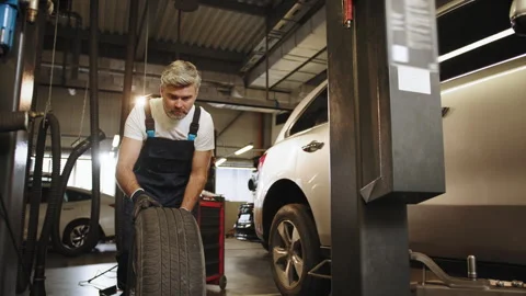 Beard handsome grey haired mature mechanic hold wheel automobile vehicle parts Stock Footage 243207254