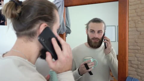 Beard man at home is Drinking a coffee looking at a mirror texting by smartphone Stock Footage 147896027