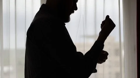 Beard man in profile silhouette buttoning his shirt in front of the window Stock Footage 93079112