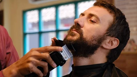 Beard styling. Barber shaping beard of handsome man using a trimmer. Skilled 스톡 동영상 129728817