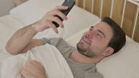 Beard Young Man doing Video Chat on Smartphone in Bed Stock-Footage 124228443