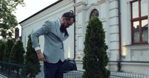 Bearded and elegantly dressed businessman, bends over and arranges his pants Video stock 140199094