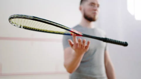 Bearded athlete spins racket on index finger in squash court Stock Footage 221002986