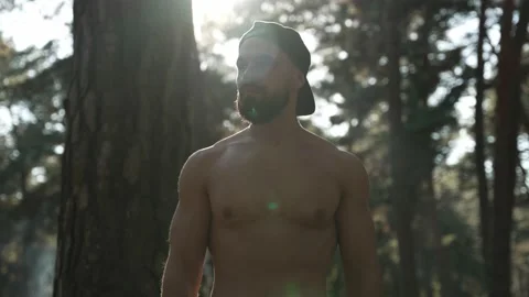 A bearded, athletic man with a bare torso is walking through the forest Stock Footage 224068691