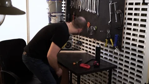 A bearded bald worker in a black T-shirt finishes his work in his workshop Stock Footage 120417471