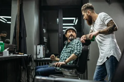 Bearded barber looking at his client while talking to him Stock Photos