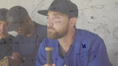 Bearded baseball player holding bat in dugout, teammates checking glove and Stock Footage 333078528