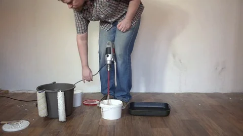 A bearded blonde man interferes paint in a bucket by a construction mixer Stock Footage 74663506