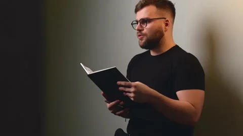 Bearded boy is reading something from the book to somebody sitting on a gray Stock Footage 146212129