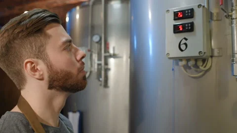 Bearded brewer man on a background of beer tanks and a brewery making notes in a Stock Footage 99977942