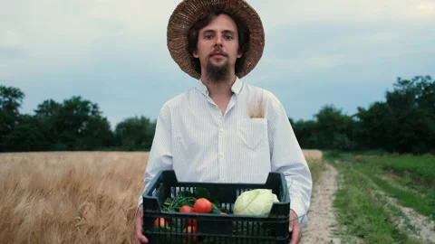 A bearded, brutal 30-year-old farmer with a hat walks in a field and carries a Vídeo Stock 133832866