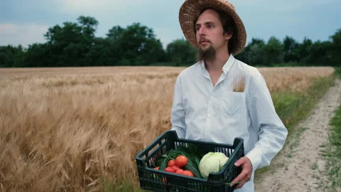 A bearded, brutal 30-year-old farmer with a hat walks in a field and carries a Stock Footage 134843000