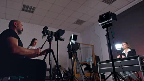 Bearded cameraman sits behind the camera recording a woman at desk.  Stock Footage 310790512